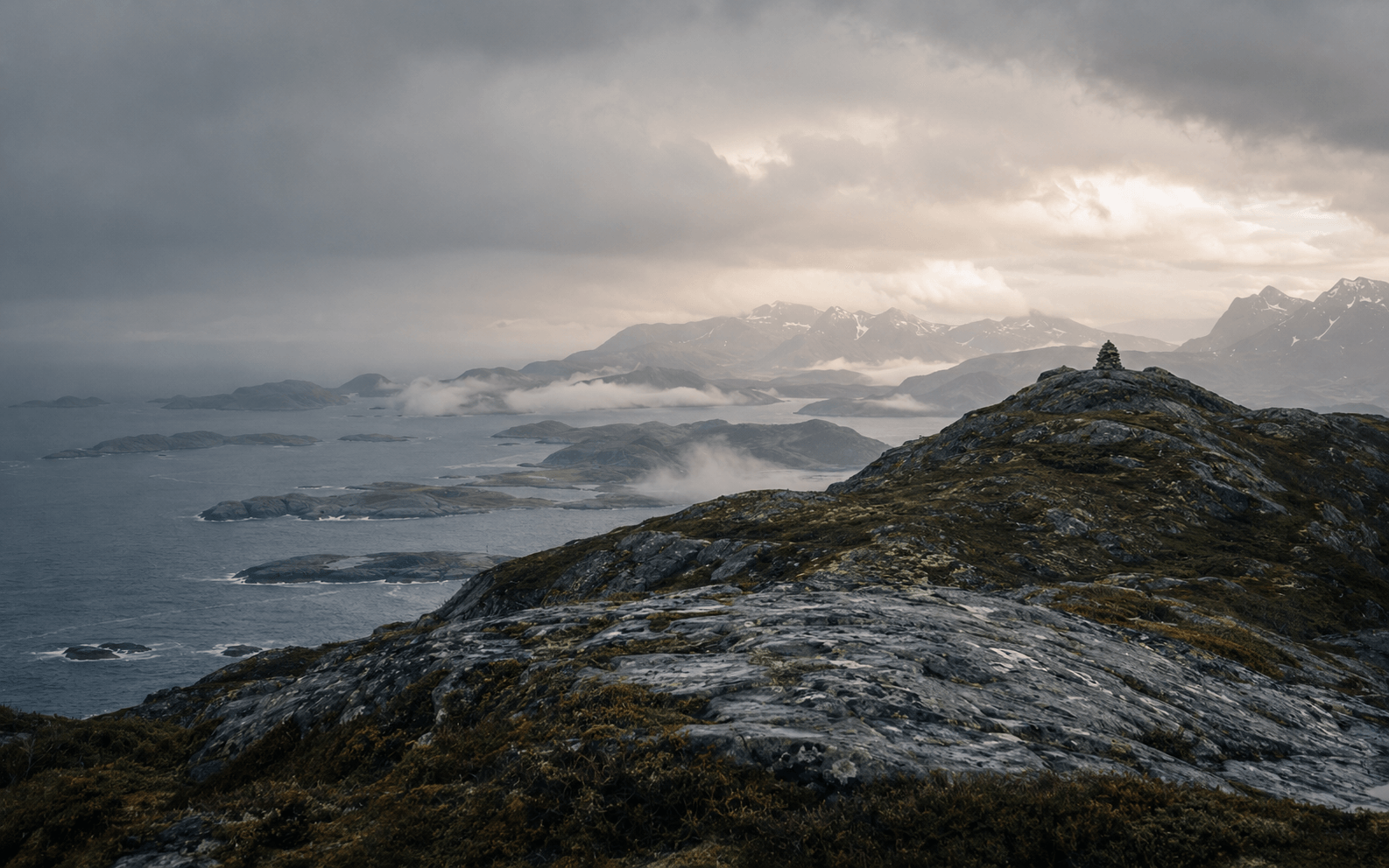 Utsikt over nordnorsk kystlandskap med fjell, holmer og en steinvarde